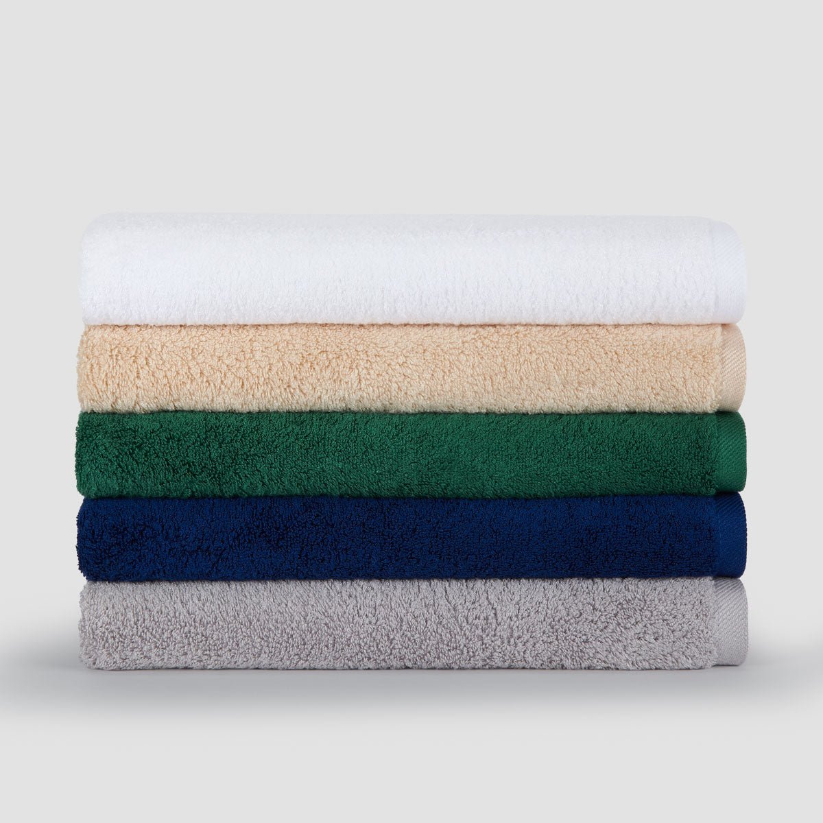Pila de cinco toallas de bambú dobladas en blanco, beige, verde, azul marino y gris sobre fondo claro.