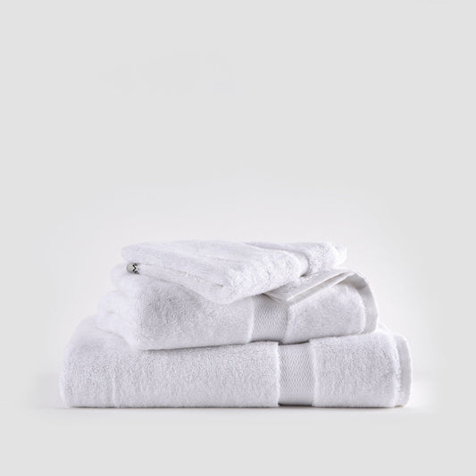 Juego de toallas de bambú blanco apiladas ordenadamente mostrando toallas faciales, de mano y baño con bandas texturadas.