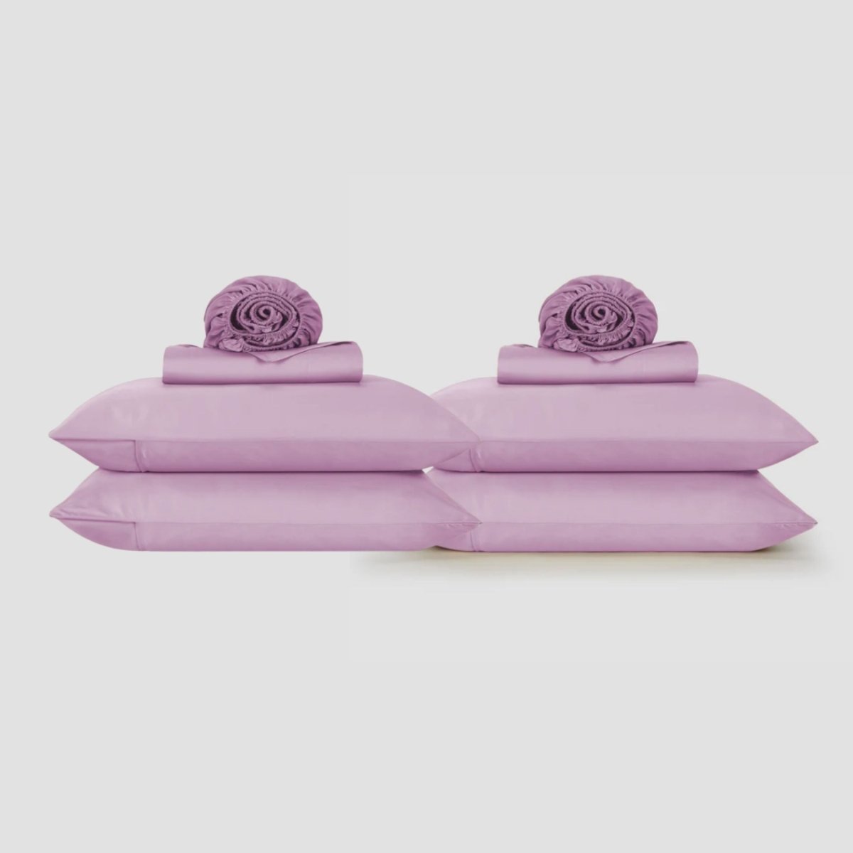 Sábanas lavanda púrpura exhibidas en plano con fundas de almohada a juego y elementos decorativos enrollados sobre fondo neutro