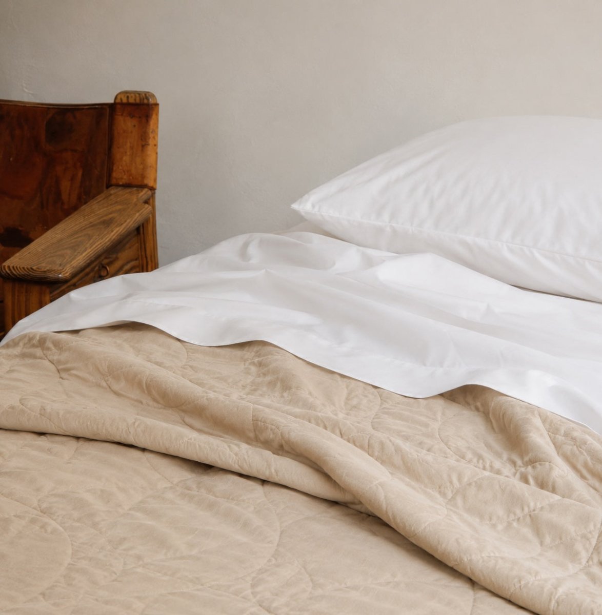 Colcha de verano acolchada beige en capas sobre sábanas blancas con almohadas en cama de madera