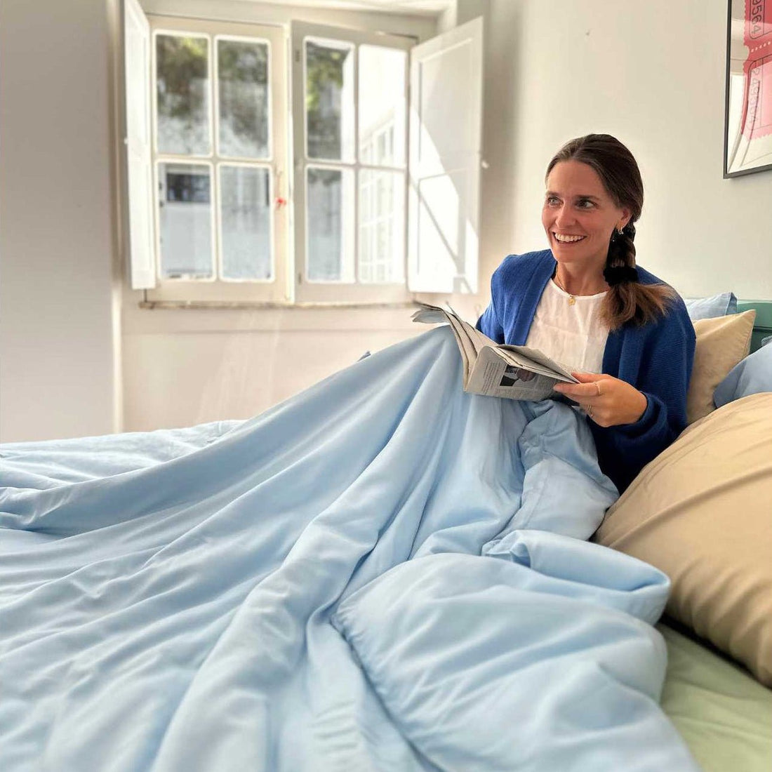 Mujer en la cama leyendo periódico con juego de cama azul claro y almohadas