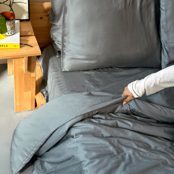 Mujer tocando ropa de cama de bambú gris en cama con mesa de madera al fondo