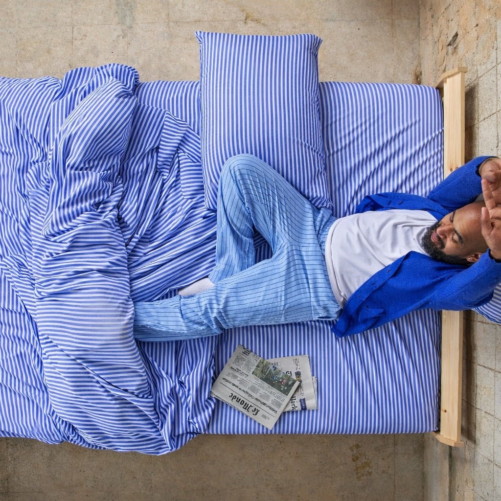 Man sleeping comfortably on blue and white striped bamboo sheets.