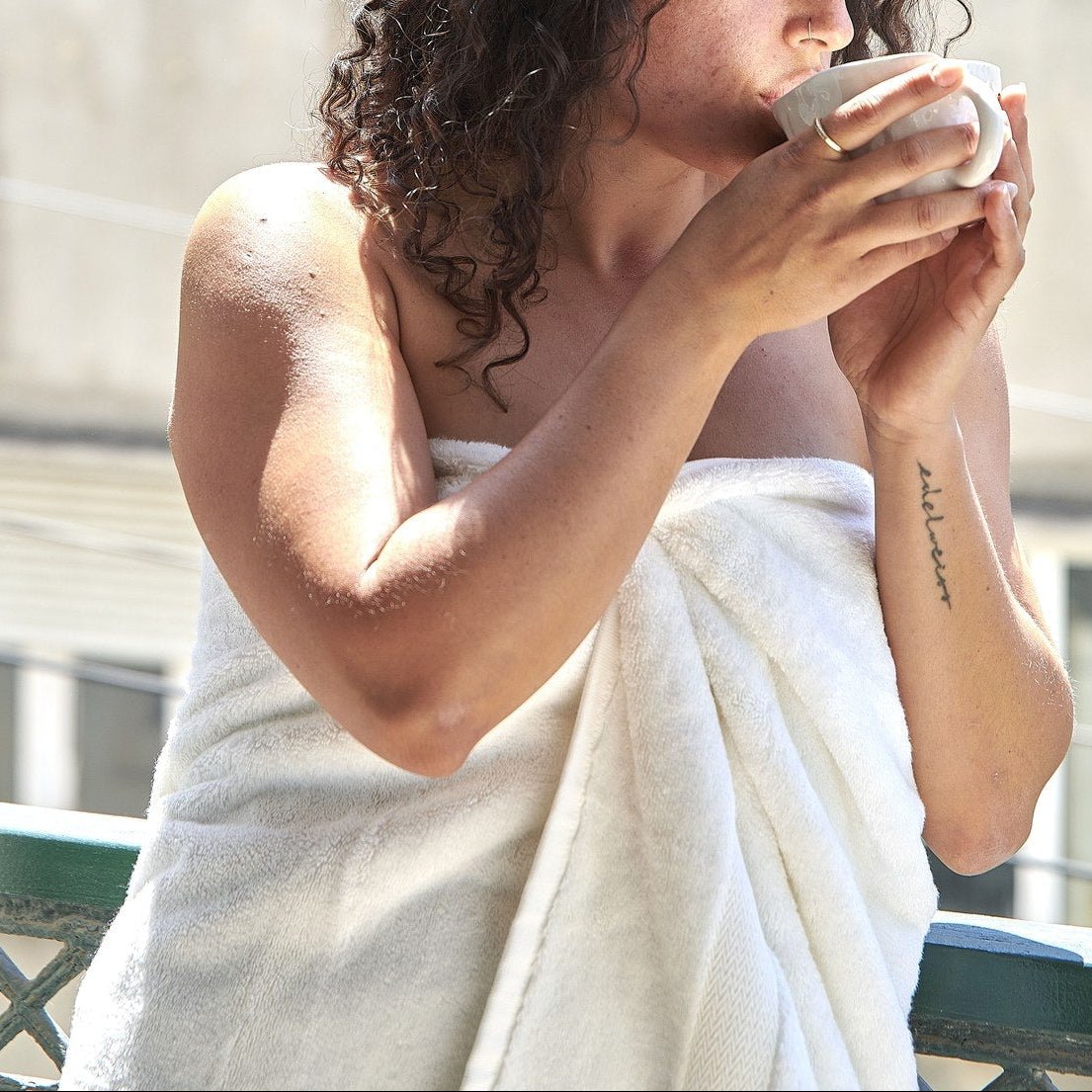 Mujer sosteniendo taza de toalla de bambú blanco al aire libre, mostrando la textura suave y calidad del set de toallas Alba