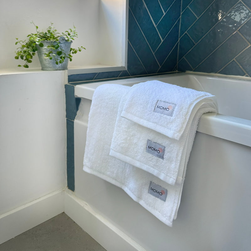 Three-piece white bamboo towel set by bathtub – bath, hand and face towels, soft, absorbent and sustainable