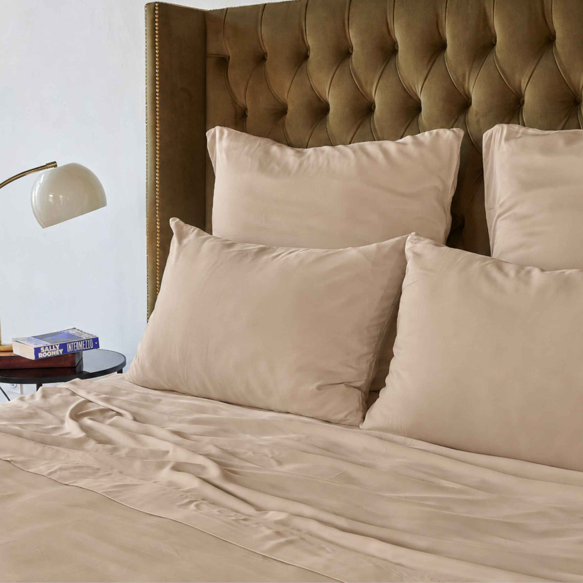 Sábana superior color crema en cama con cabecera tapizada marrón y almohadas beige