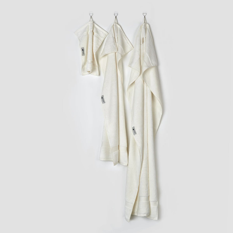 Tres toallas de bambú crema colgadas en ganchos mostrando tamaños cara, mano y baño de la colección Alba por momo-cotton