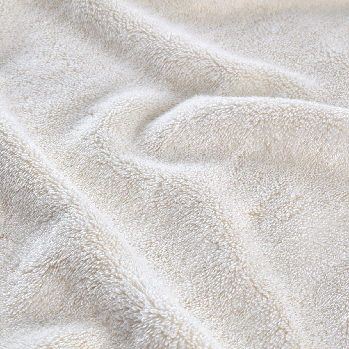 Juego de toallas de bambú color crema dobladas y apiladas, mostrando textura suave y detalle de fibras naturales