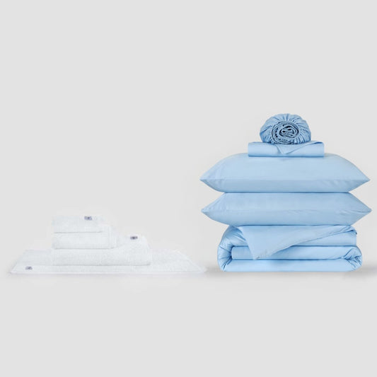 Juego de cama azul y blanco con almohadas y sábanas dobladas sobre fondo blanco