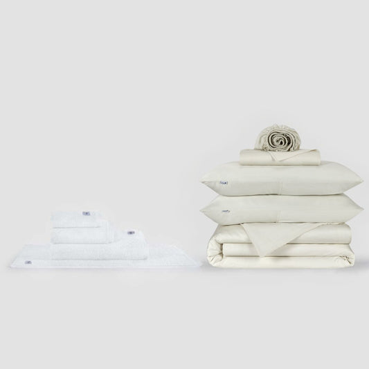 Juego de sábanas completo Momo Cotton y colección de toallas en crema, mostrando ropa de cama y toallas dobladas sobre fondo blanco