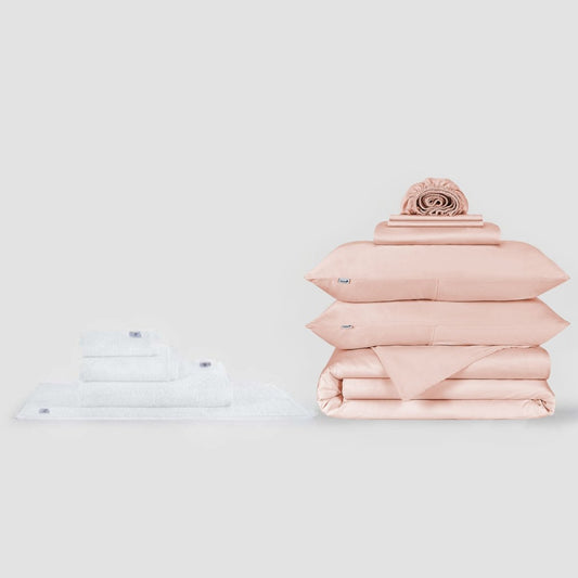 Juego de toallas blancas y sábanas rosa con almohada decorativa sobre fondo neutro de Momo Cotton