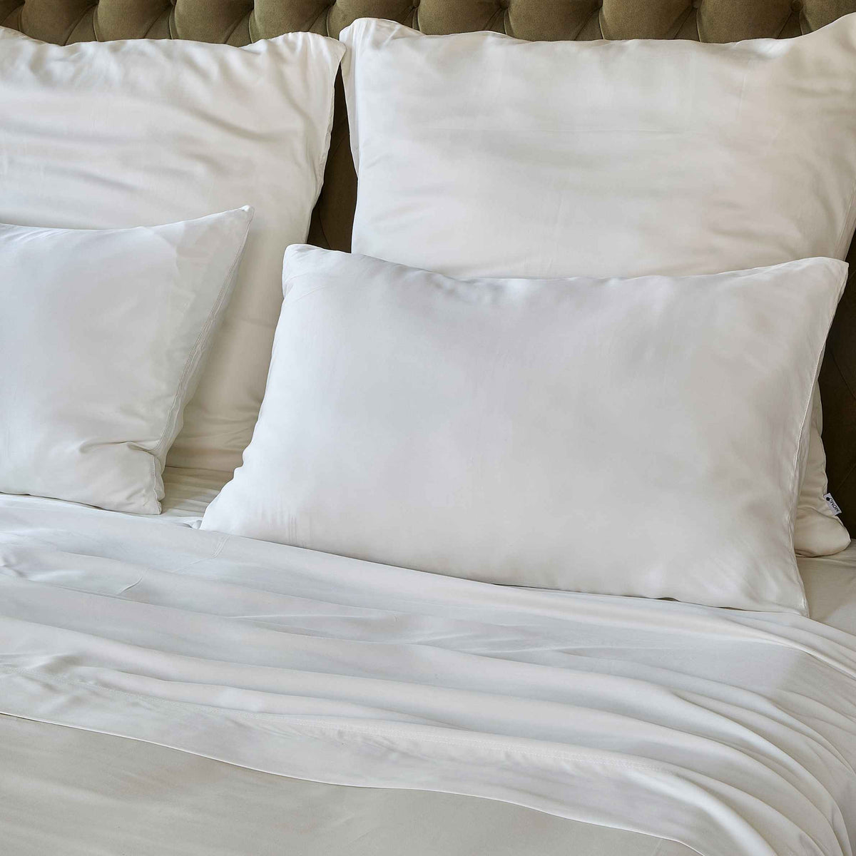 Sábana blanca sobre cama con almohadas y cabecero tapizado beige