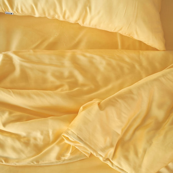 Juego de ropa de cama de bambú crema con almohadas y edredón doblados, mostrando textura suave y trama de calidad