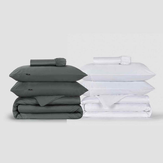 Dos juegos de fundas nórdicas Momo Cotton lado a lado, uno gris carbón y otro blanco, apilados con almohadas