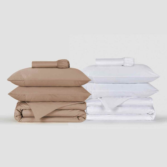 Juegos de funda nórdica beige y blanca apilados mostrando ropa de cama doblada con almohadas y sábanas de Momo Cotton