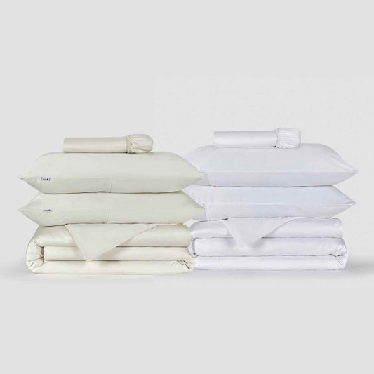 Juegos de ropa de cama crema y blanca con fundas de edredón, almohadas y sábanas dobladas sobre fondo blanco