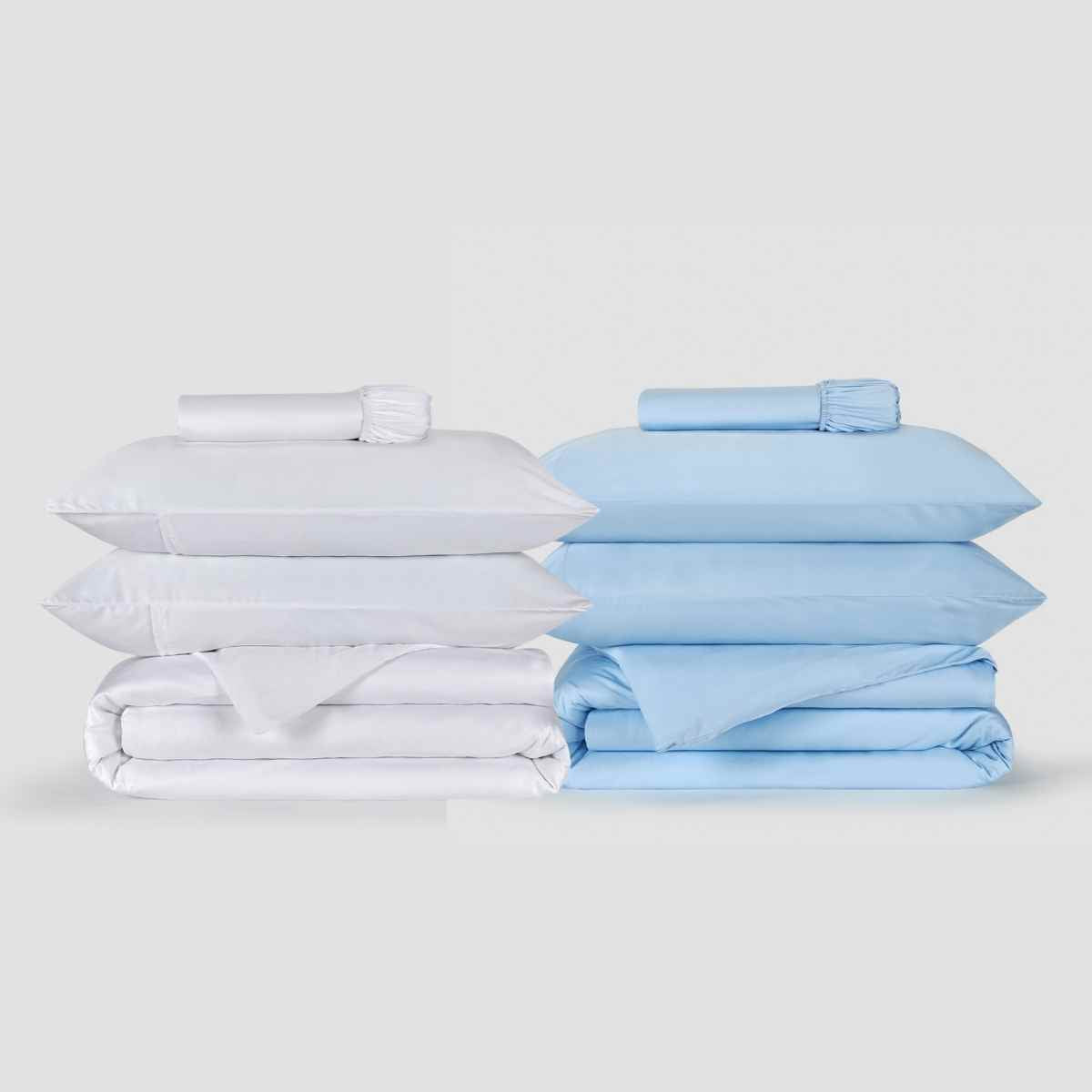 Conjuntos de roupa de cama empilhados em branco e azul céu, com lençóis, fronhas e edredão dobrados, apresentados de forma minimalista e elegante.