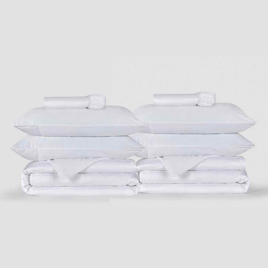 Dos juegos de fundas nórdicas blancas apilados con almohadas y ropa de cama Momo Cotton sobre fondo neutro