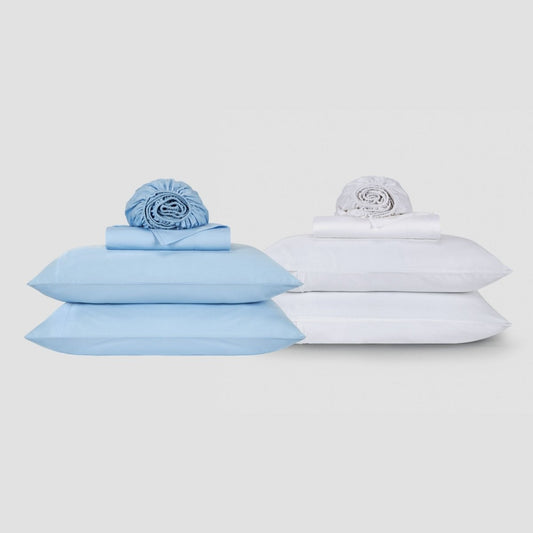 Juego de sábanas azul y blanco de algodón con almohadas y ropa de cama enrollada sobre fondo neutro