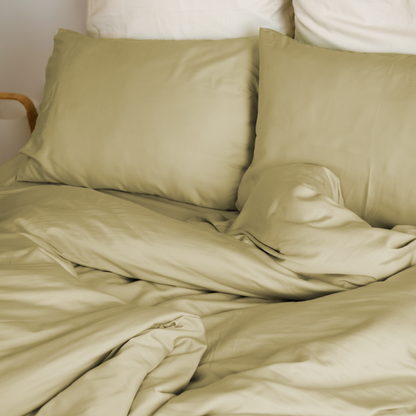 Cama com capa de edredão bege areia, almofadas bege e almofadas brancas atrás – macio e sustentável