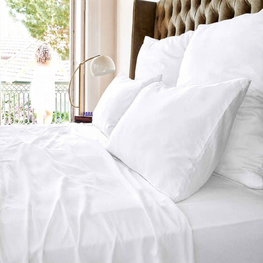 Sábana blanca superior en cama con almohadas y cabecero tapizado junto a ventana con vista al balcón