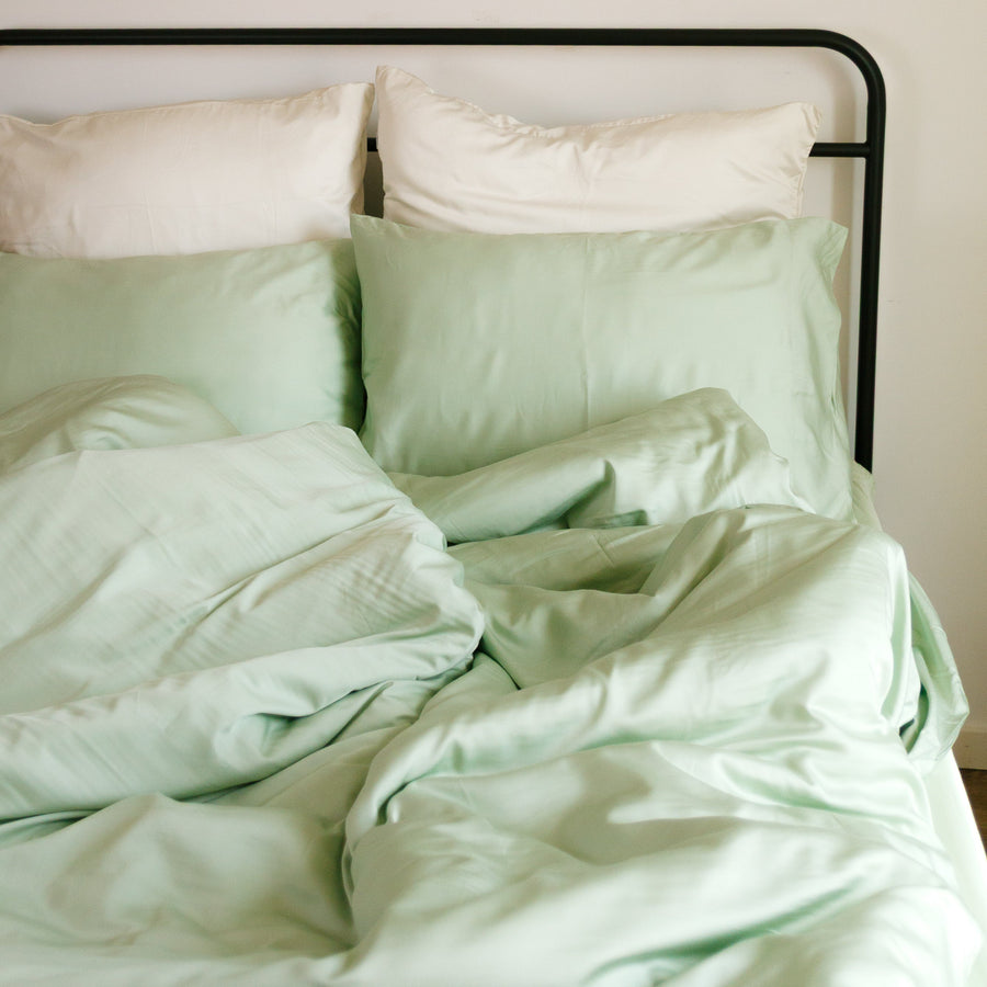 Juego de funda nórdica verde claro y blanco sobre cama con estructura negra, decoración con platos de rattan