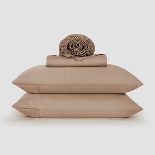 Juego de sábanas de bambú beige apilado con edredón enrollado y dos almohadas sobre fondo blanco