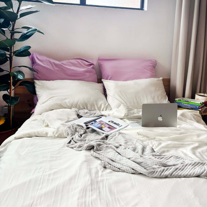 White, pearl and lilac bamboo duvet set with grey bamboo blanket on messy bed – soft, breathable and sustainable